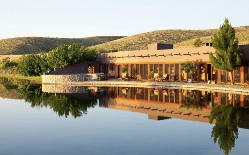 Cibolo Creek Ranch's adobe lodge and cottonwoods reflected in the still water of its lake at golden hour