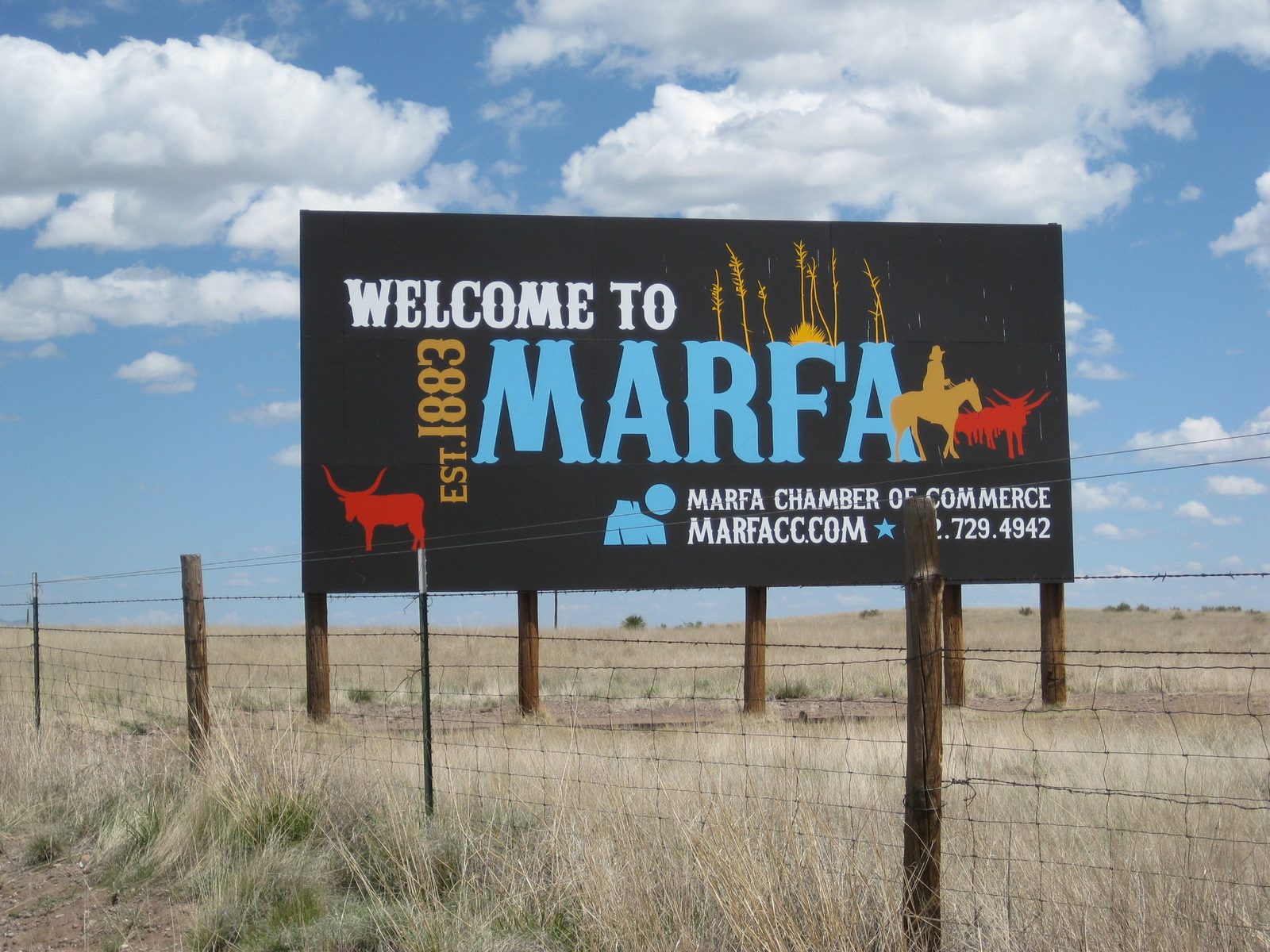 The Welcome to Marfa sign, established 1883, standing in open desert grassland under a deep blue West Texas sky